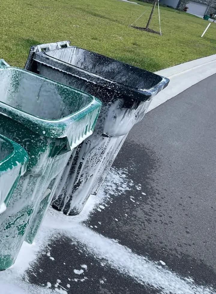 Curbside trash and recycling carts covered in cleaning foam on a suburban street